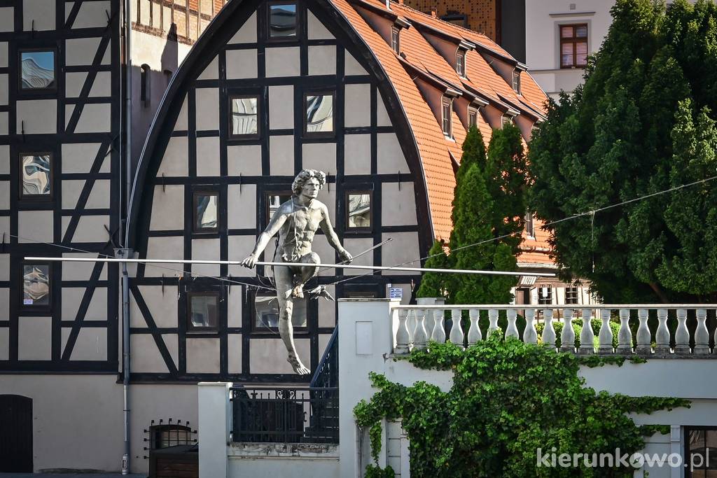 Rzeźba balansująca na tle bydgoskich spichlerzy nad Brdą